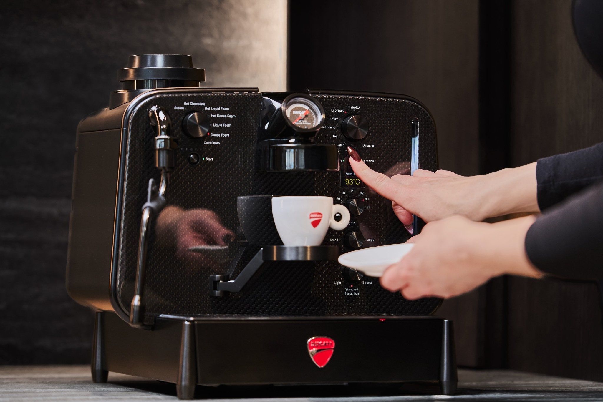Hånd starter en espresso på Barista M3 1926, 93 °C vises på displayet, Ducati-kop nedenunder