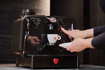 Hånd starter en espresso på Barista M3 1926, 93 °C vises på displayet, Ducati-kop nedenunder